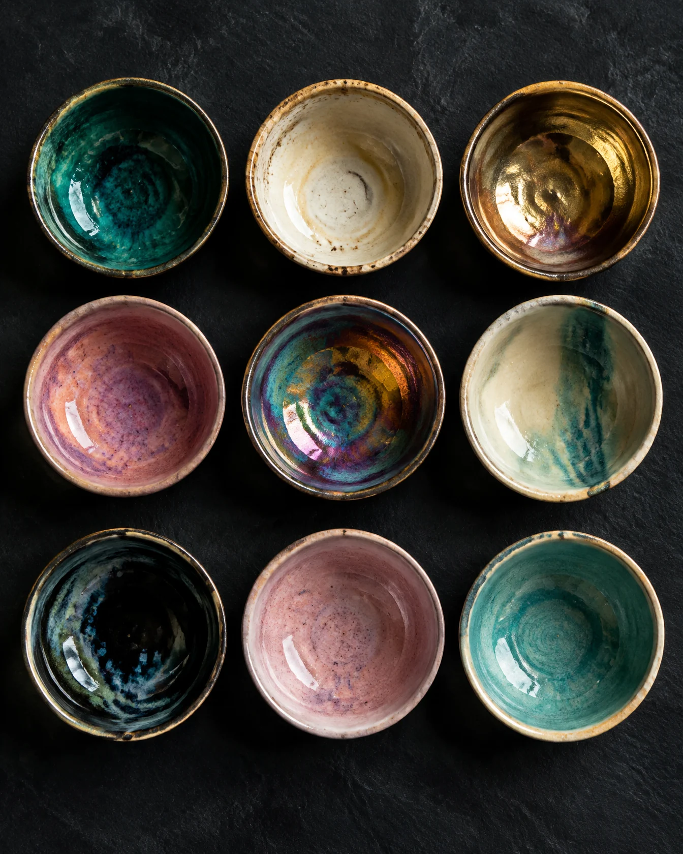 Grid of nine handmade ceramic cups in teal, cream, gold and pink glazes