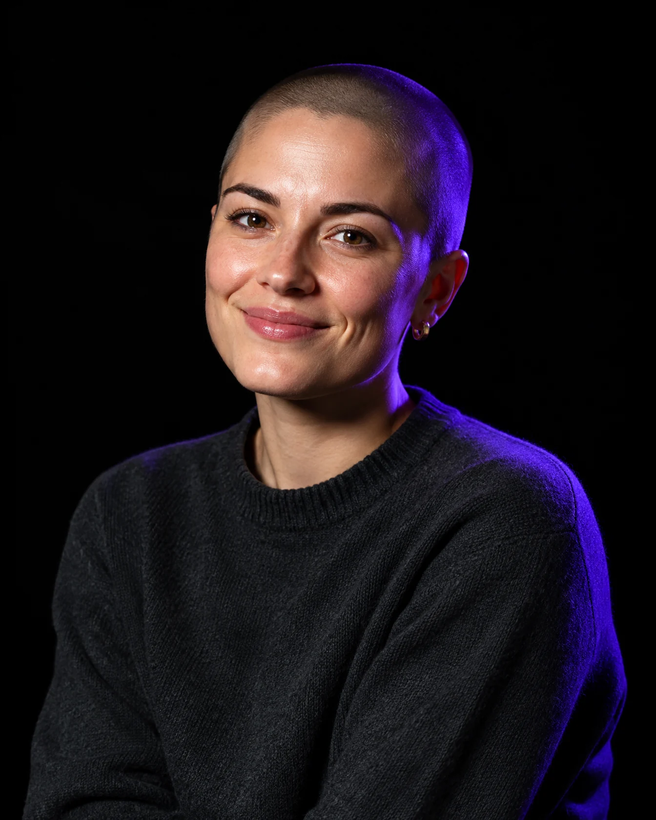Designer with a shaved head and gold earrings, violet rim light